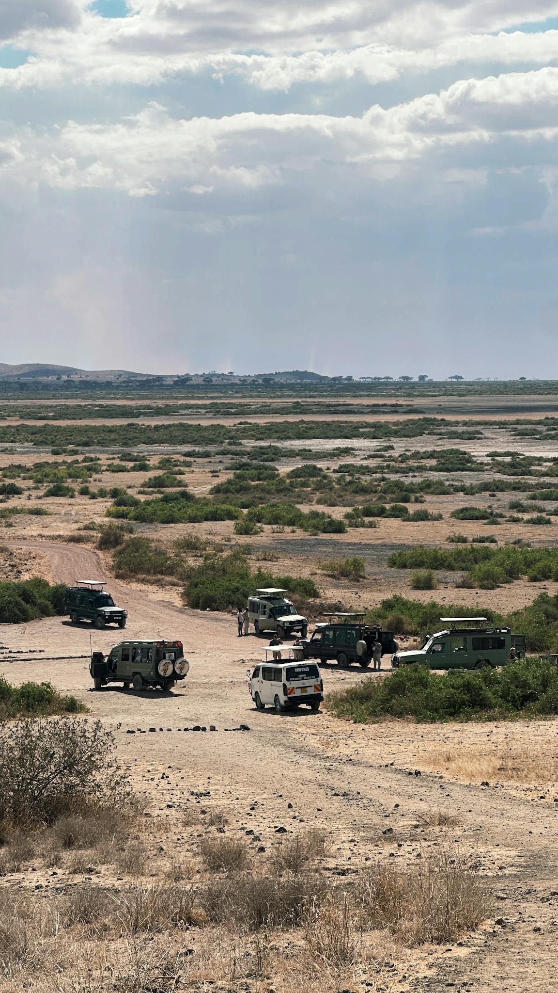 Safari vehicles traverse the rugged terrain of a vast South African landscape under a cloudy sky.
